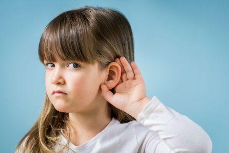 Child with hearing problem on blue background. Hearing loss in childhood, symptoms and treatment concept. Close up, copy space.